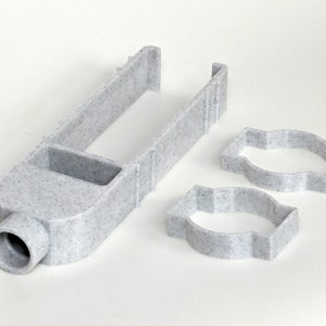 May include: A light gray, speckled plastic tool with a long, rectangular handle and a circular opening at the base. Two matching, open-sided, oval-shaped objects are also present. The items appear to be 3D-printed.