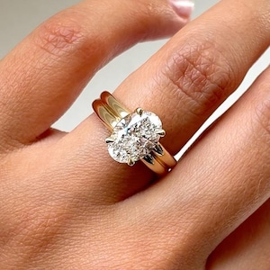 Op de afbeelding: Een gouden ring met een grote, gefacetteerde, ovaal geslepen heldere edelsteen die op zijn plaats wordt gehouden door vier pootjes. De ringband is glad, gepolijst en van massief goud, met een klassiek ontwerp dat de schittering benadrukt.