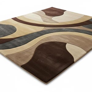 A high-angle shot of a rectangular hand-tufted wool area rug featuring a modern abstract pattern in brown, beige, tan, and grey. The rug is placed on a light oak wood floor in a bright living room next to a cream sofa, potted plants, and a wooden coffee table.