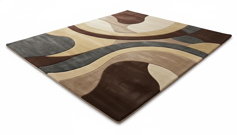 A high-angle shot of a rectangular hand-tufted wool area rug featuring a modern abstract pattern in brown, beige, tan, and grey. The rug is placed on a light oak wood floor in a bright living room next to a cream sofa, potted plants, and a wooden coffee table.