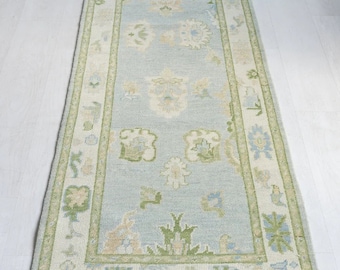 May include: A light blue runner rug with a green and white floral pattern. The rug has a fringe border.