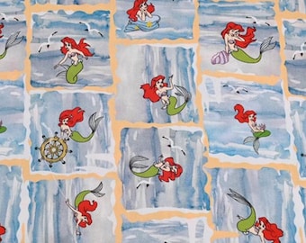 May include: A repeating pattern of a mermaid with red hair and a green tail. The mermaid is in various poses, including swimming, holding a seashell, and steering a ship's wheel. The background is a watercolor-style design of blue and white waves.