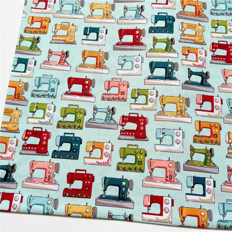 May include: A teal fabric with a repeating pattern of colorful sewing machines. The sewing machines are in various colors, including red, yellow, blue, green, and pink. Each sewing machine has a floral design around it.