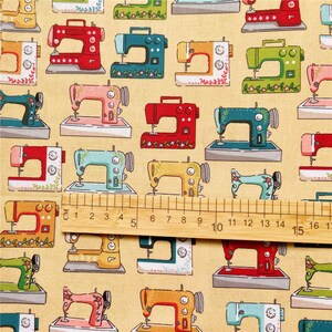 May include: A beige fabric with a repeating pattern of colorful sewing machines. The sewing machines are in various colors, including red, blue, green, yellow, and pink. The fabric has a ruler with markings in inches.