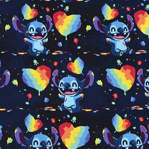 Puede incluir: Un personaje de dibujos animados azul con ojos grandes y una amplia sonrisa sostiene un corazón arcoíris. El fondo es azul oscuro con salpicaduras de pintura blanca.