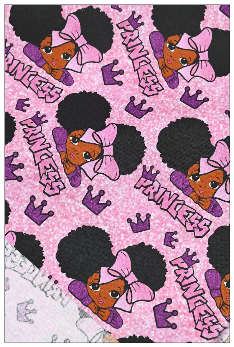 May include: Pink fabric with a repeating pattern of a black girl with an afro, a pink bow, and the word "Princess" in purple. The background is a sparkly pink.