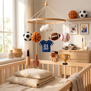 May include: A sports-themed nursery mobile featuring a circular wooden frame with hanging felt ornaments including a soccer ball, basketball, football, baseball, a blue jersey with 01 MVP text, a baseball bat, a foam finger with #1 text, and a trophy.