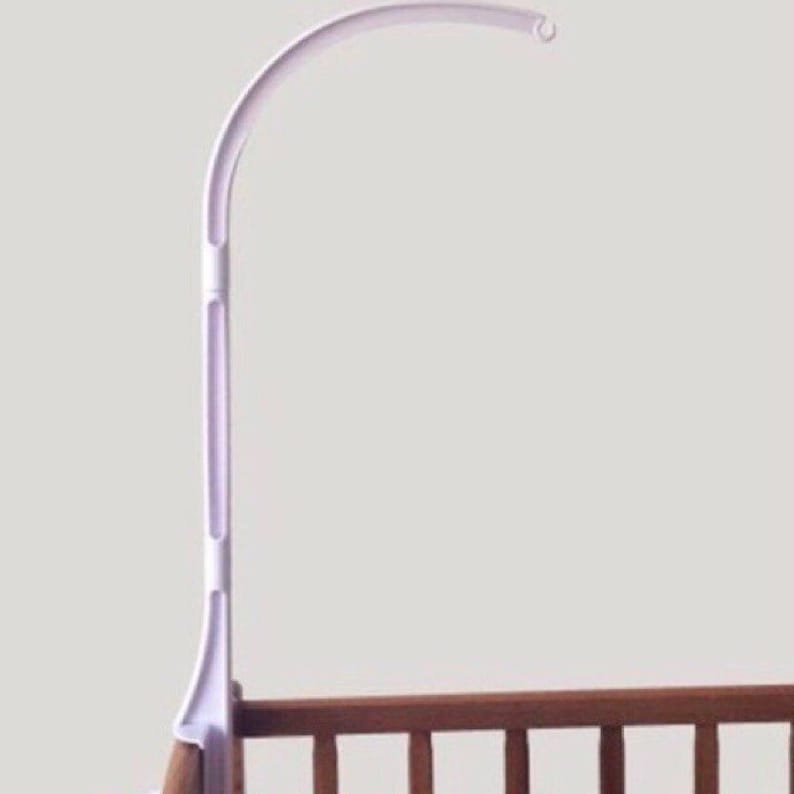 May include: White plastic baby crib mobile arm with a curved arm and a hook at the end. The arm is attached to a base that can be clamped to the side of a crib.