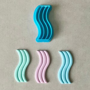 May include: A collection of wavy-shaped cookie cutters in various colors. The top cutter is bright blue, while the others are mint green, light pink, and a lighter blue. The cutters are made of plastic and are designed for baking.