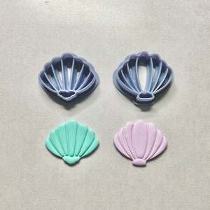May include: Two blue plastic cookie cutters shaped like seashells, and two fondant seashells, one light green and one light purple.