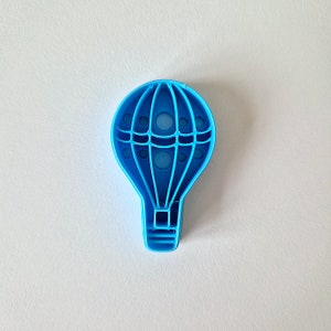 May include: A light blue plastic cookie cutter shaped like a hot air balloon. The balloon has a basket and a grid pattern.