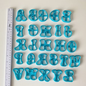 Könnte beinhalten: Ein Satz mit 26 blauen Plastik-Ausstechern in Form von Buchstaben des Alphabets. Die Ausstecher sind in alphabetischer Reihenfolge angeordnet.