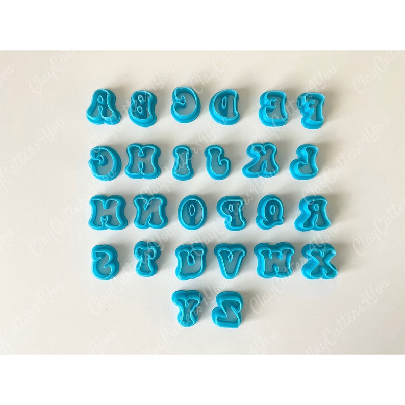 May include: A set of 26 blue plastic alphabet cookie cutters in a retro style font. The cutters are arranged in alphabetical order on a white surface.