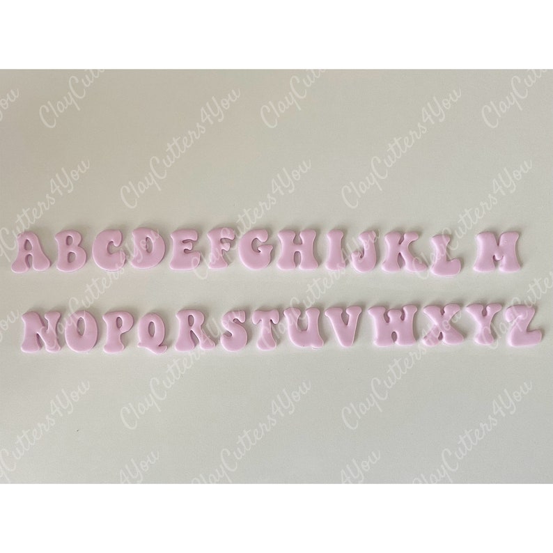 May include: Pink alphabet letter cookie cutters. The letters are in a stylized font and are arranged in two rows. The letters are A through Z.
