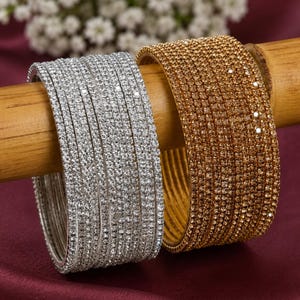 May include: A set of silver-toned bangles and a set of gold-toned bangles, each featuring multiple rows of small, clear, reflective crystals embedded across the entire surface of the circular metal bands, creating a highly textured appearance.