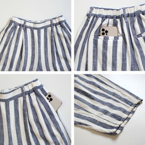 May include: Close-up shots of blue and white striped shorts. The shorts have a comfortable elastic waistband and pockets. A smartphone is visible in one of the pockets. The fabric appears to be a lightweight linen or cotton blend.
