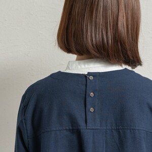 May include: A navy blue shirt with a round neckline and a row of five buttons down the back.