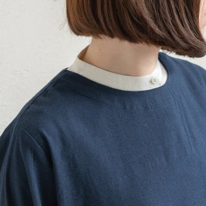 May include: A navy blue shirt with a white collar and a single button closure. The shirt has a relaxed fit and a round neckline.