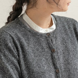 May include: A gray cardigan with a white collared shirt underneath. The cardigan has a button-up front and a textured knit.