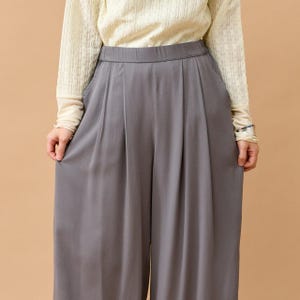 Puede incluir: Pantalones grises de pernera ancha con pliegues en la cintura. Los pantalones est&aacute;n hechos de una tela suave y fluida. La persona lleva una camiseta crema de manga larga.