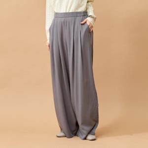 Puede incluir: Pantalones grises de pernera ancha con cintura alta y pliegues. Los pantalones tienen bolsillos y un ajuste holgado y relajado. La modelo lleva una camisa de manga larga color crema. Los pantalones son de tejido suave y fluido.