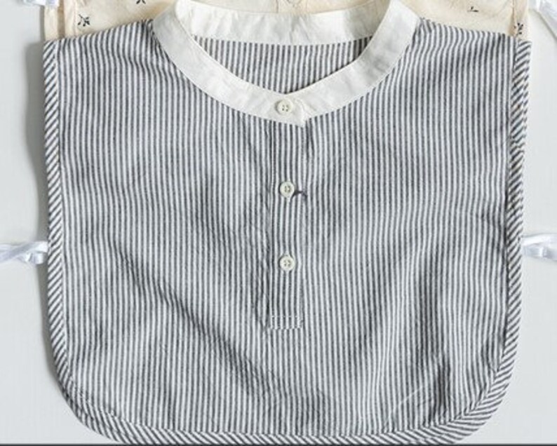 May include: A white and black striped cotton bib with a rounded neckline and three buttons down the front.