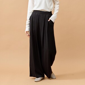 Puede incluir: Pantalones negros de pernera ancha, cintura alta y bolsillos. Se combinan con una camisa blanca de manga larga. Los pantalones tienen un corte holgado y relajado, adecuado para el uso diario.