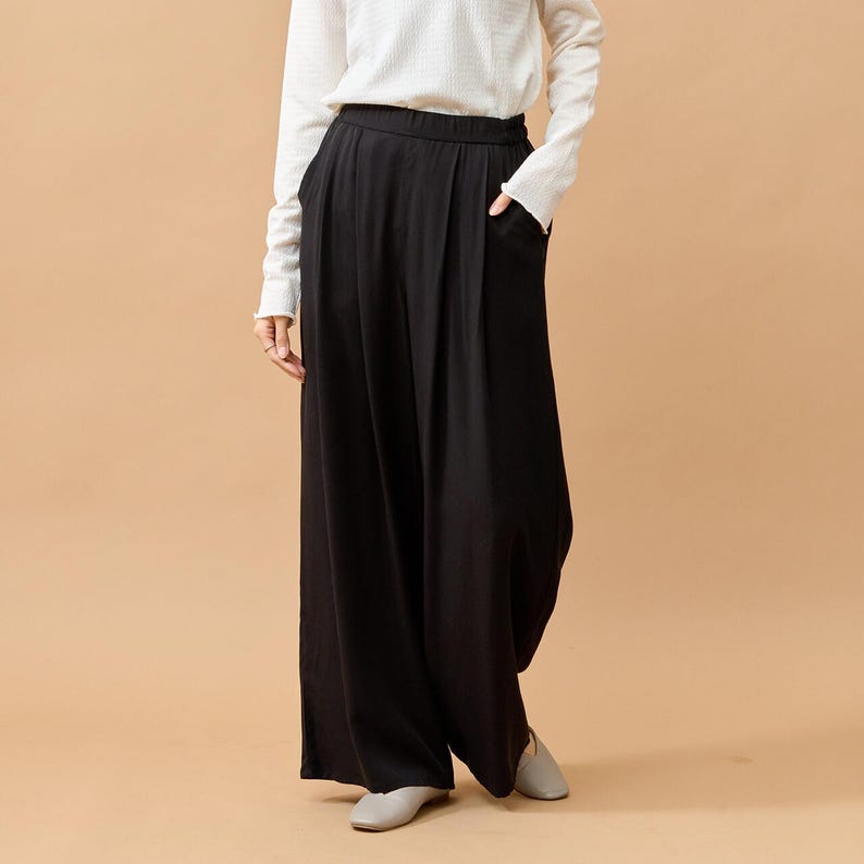 Puede incluir: Pantalones negros de pernera ancha, cintura alta y bolsillos. Se combinan con una camisa blanca de manga larga. Los pantalones tienen un corte holgado y relajado, adecuado para el uso diario.