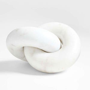 Puede incluir: Escultura de mármol blanco con diseño de nudo. La escultura tiene una superficie lisa y pulida y está sobre un fondo blanco. La forma entrelazada crea una estética moderna y minimalista, adecuada para la decoración del hogar.