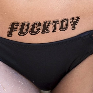FUCKTOY, tatuaggio BDSM malizioso e vizioso in nero per impressionare. Ti piace essere sfruttato per i desideri sessuali?