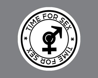 May include: A circular sticker with a white background and a black border. The text "TIME FOR SEX" is printed twice along the inner edge, separated by two asterisks. In the center, a black combined male and female gender symbol is displayed.