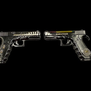 Può includere: Due pistole giocattolo argentate sono esposte su sfondo nero. Una pistola ha la scritta "CONSECRATED SOLDIERS" e l'altra "BABA YAGA". Le impugnature presentano elementi decorativi.