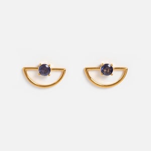 Può includere: Un paio di orecchini color oro, ciascuno con un design a semicerchio e una piccola gemma rotonda blu scuro al centro. Gli orecchini sono su uno sfondo bianco, evidenziando il loro stile minimalista ed elegante.