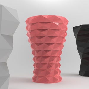 May include: Three geometric vases in different colors and designs. The vase on the left is gray, the vase in the center is pink, and the vase on the right is black.