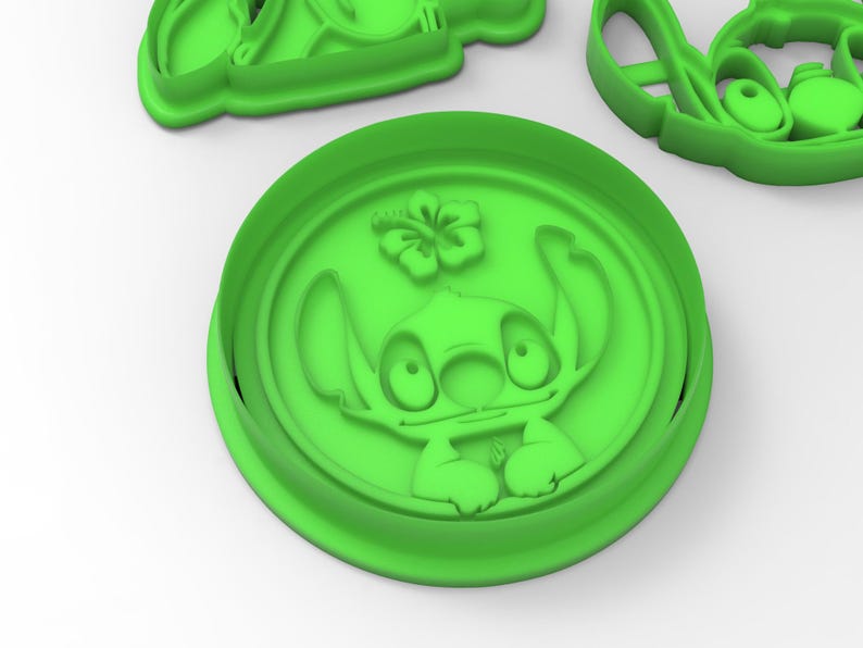 May include: Green plastic cookie cutter featuring a cartoon character with large eyes and a flower. The character is Stitch from the Disney movie Lilo & Stitch.