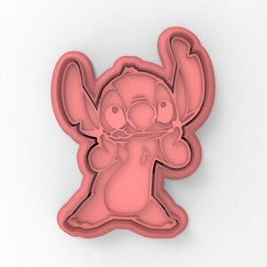 May include: Pink plastic cookie cutter shaped like Stitch from the Disney movie Lilo & Stitch. Stitch is shown with his signature wide eyes and goofy grin.