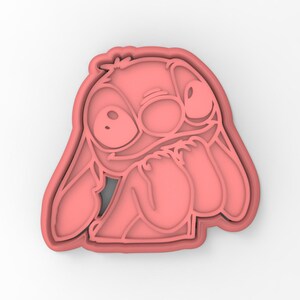 May include: Pink plastic cookie cutter shaped like Stitch from the Disney movie Lilo & Stitch. Stitch is shown with his signature blue eyes and a mischievous expression.