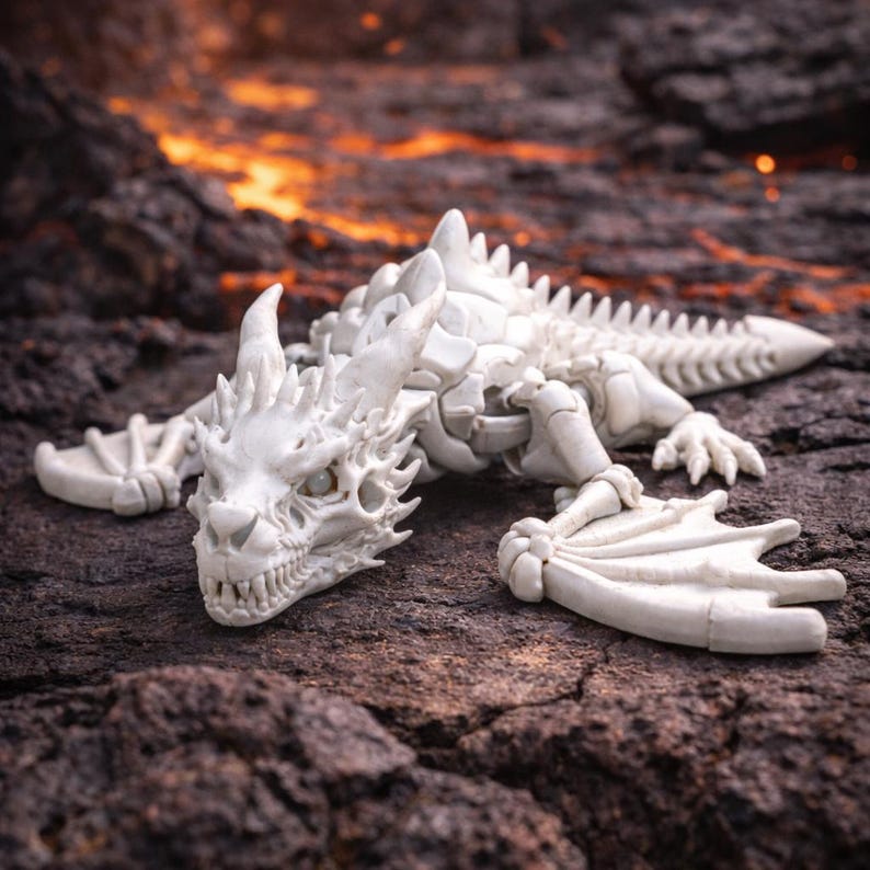 May include: A detailed, off-white dragon figurine with a skeletal design, featuring horns, wings, and sharp teeth. The dragon is lying on a dark, textured surface with an orange and red background, creating a fantasy theme.