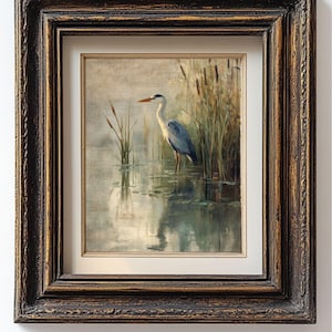 May include: A framed painting of a grey heron standing in a pond with reeds in the background. The heron is facing to the right and has its head turned to the left. The painting is done in a realistic style and has a muted color palette.