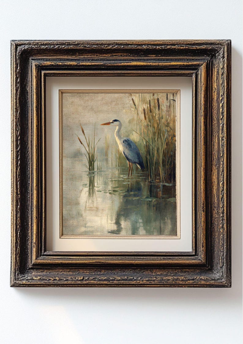 May include: A framed painting of a grey heron standing in a pond with reeds in the background. The heron is facing to the right and has its head turned to the left. The painting is done in a realistic style and has a muted color palette.