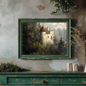 Op de afbeelding: Een ingelijst schilderij van een wit kasteel met een rood dak, omringd door bomen en mist. Het schilderij is in een groene lijst en hangt aan een muur.
