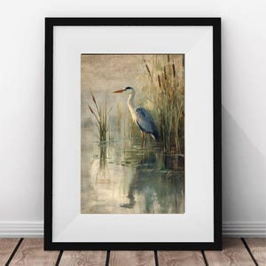 May include: A framed painting of a gray heron standing in a pond with reeds in the background. The heron is facing to the left and has its head turned to the right. The water is a light blue color and the reeds are a light brown color.
