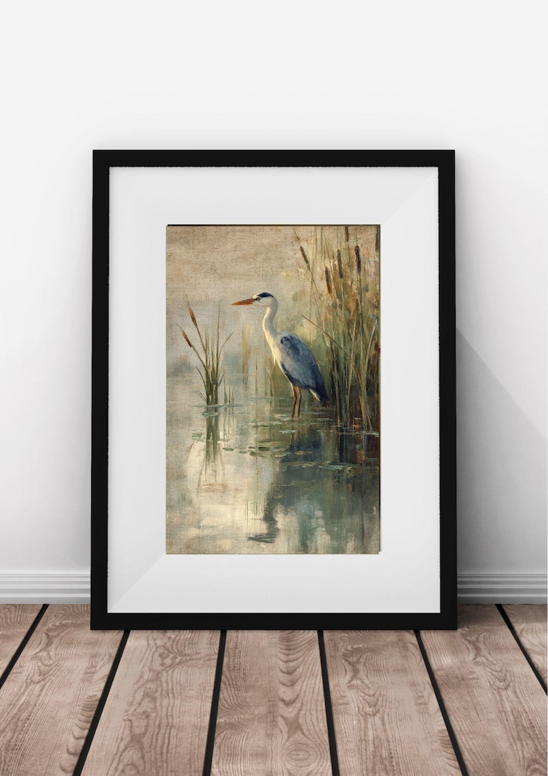 May include: A framed painting of a gray heron standing in a pond with reeds in the background. The heron is facing to the left and has its head turned to the right. The water is a light blue color and the reeds are a light brown color.