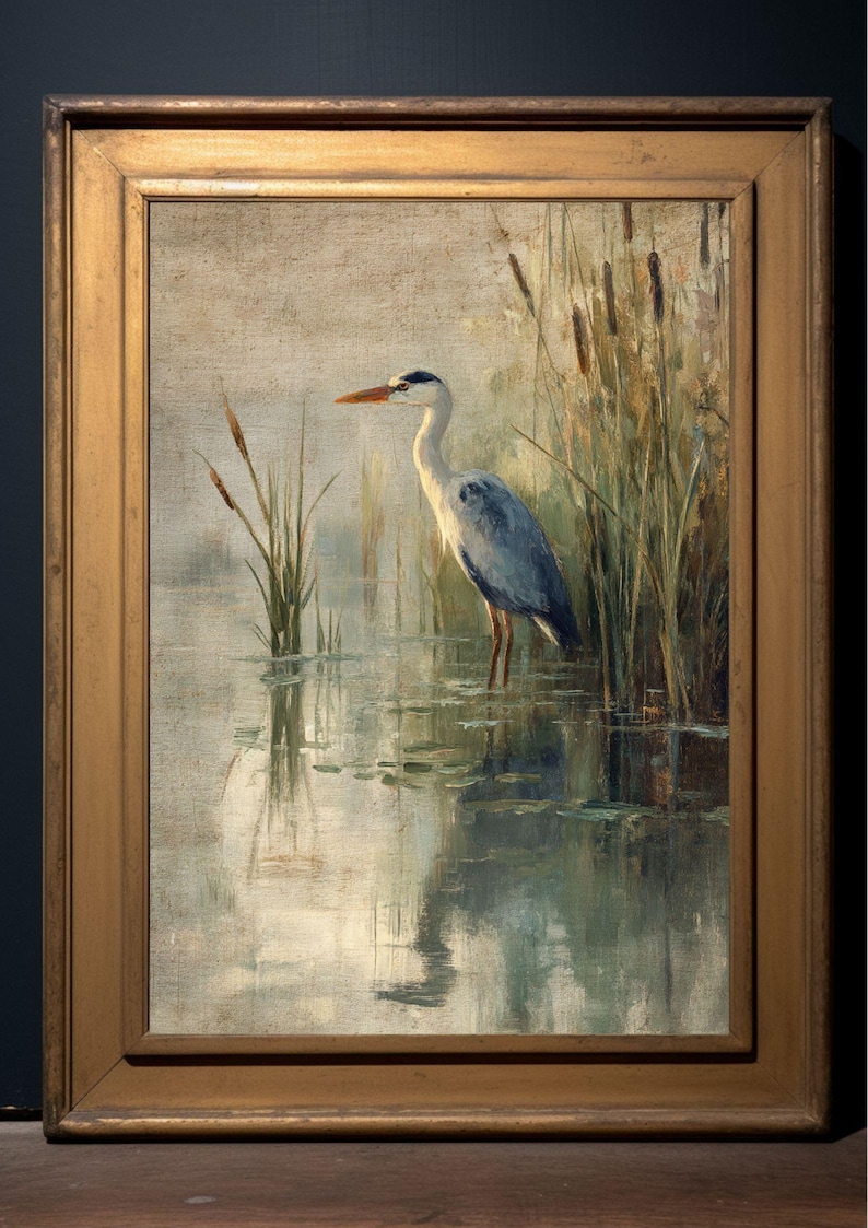 May include: A framed oil painting of a grey heron standing in a pond with reeds in the background. The heron is facing left and has its head turned to the right. The water is a light blue-green color and the reeds are a dark green color.