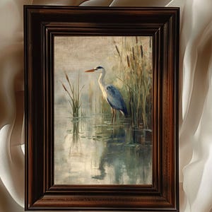 May include: A framed painting of a grey heron standing in a pond with reeds in the background. The heron is facing to the left and has its head turned to the right. The water is a light blue color and the reeds are a dark green color.