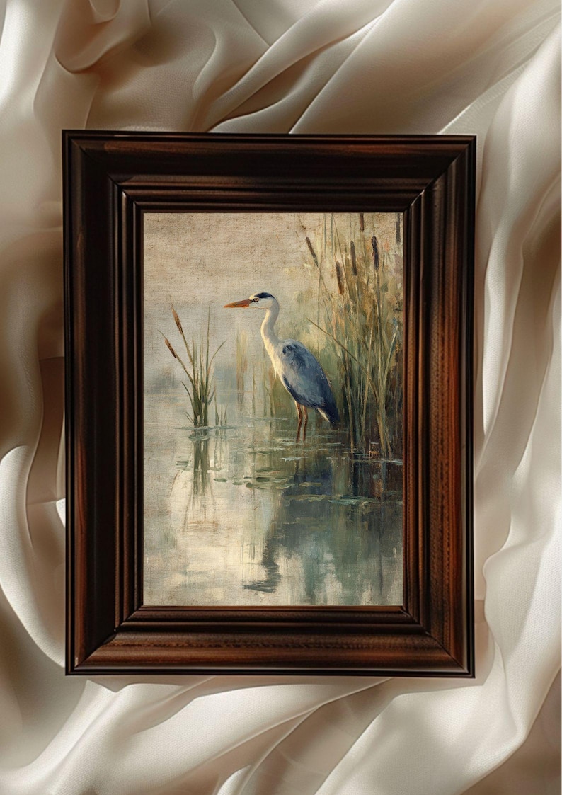 May include: A framed painting of a grey heron standing in a pond with reeds in the background. The heron is facing to the left and has its head turned to the right. The water is a light blue color and the reeds are a dark green color.