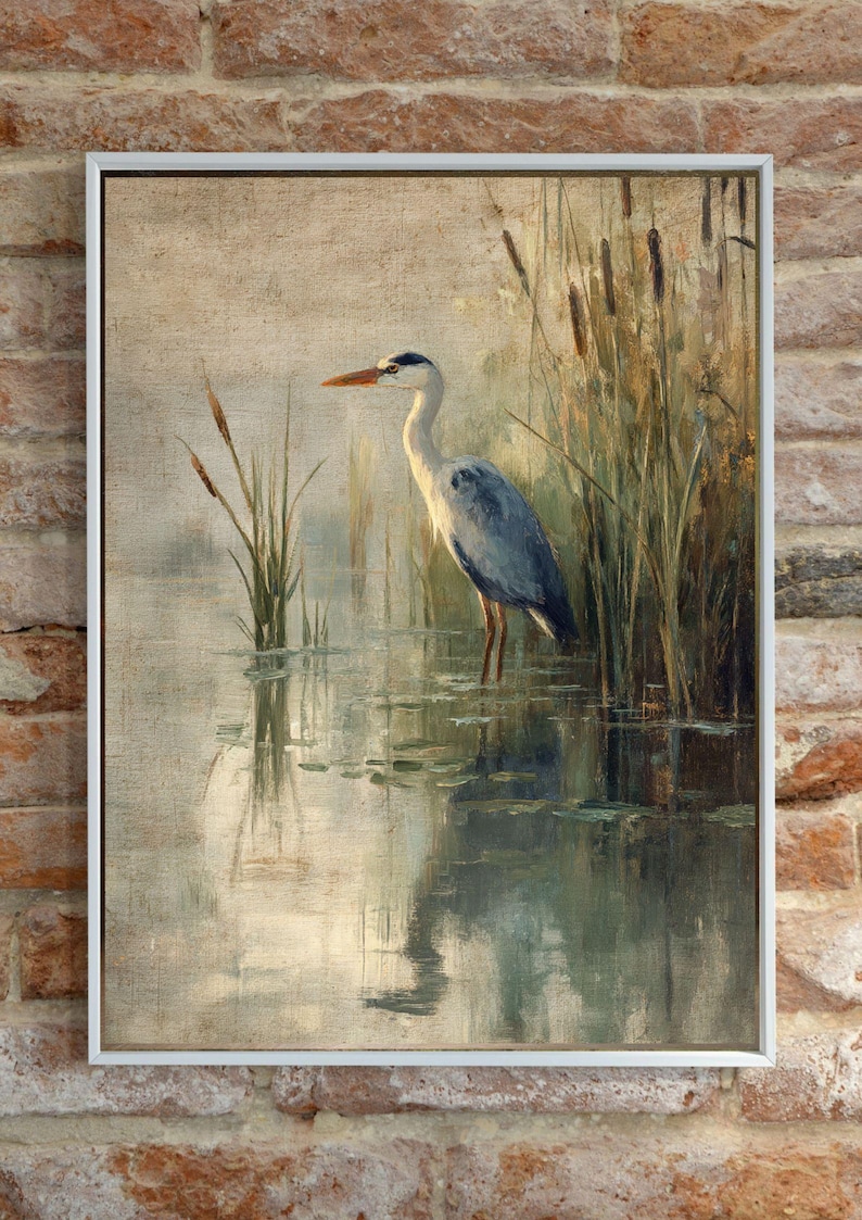 May include: A framed painting of a grey heron standing in a pond with reeds in the background. The heron is facing to the left and has its head turned to the right. The water is a light blue-green color and the reeds are a light brown color.