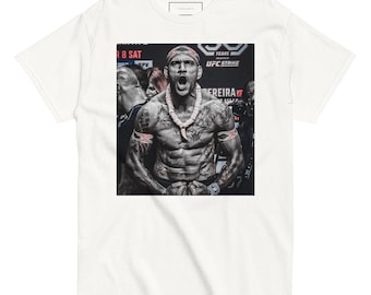 Op de afbeelding: Wit t-shirt met een zwart-wit afbeelding van een gespierde persoon met tatoeages, een ketting en een hoofdband, schreeuwend. De afbeelding staat tegen een vage achtergrond met de tekst "UFC Strike".