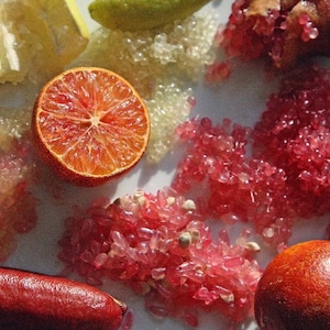 Puede incluir: Un plato blanco con varias frutas cítricas y sus cáscaras, incluyendo una naranja roja, una lima verde y una lima de dedo. El plato también contiene caviar de cítricos rosa y blanco.
