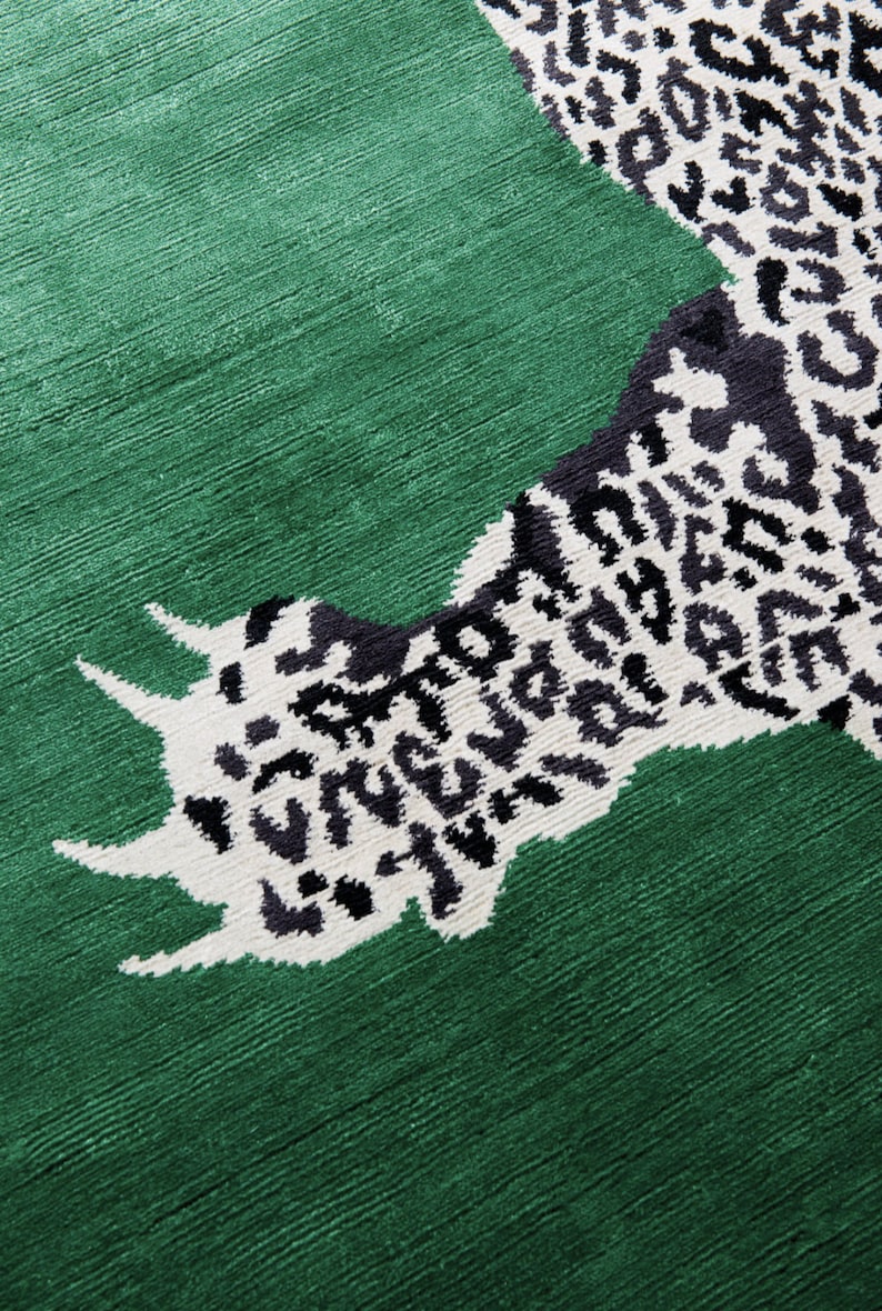 Pu&ograve; includere: Un tappeto verde con un design sorprendente. Il tappeto presenta una grande impronta stilizzata in un motivo leopardato bianco e nero. Lo sfondo &egrave; verde pieno e strutturato.